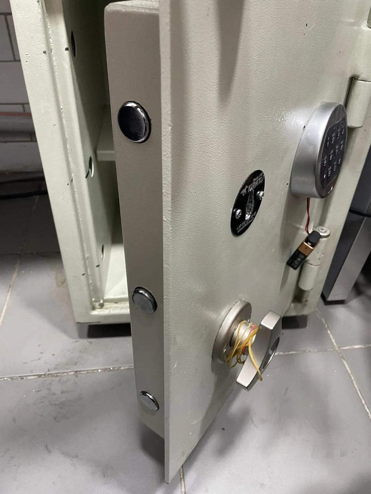Açılmış Kıratlı çelik kasanın kapak kenarında üç adet krom sürgü pimi, marka rozeti ve elektronik tuş takımı