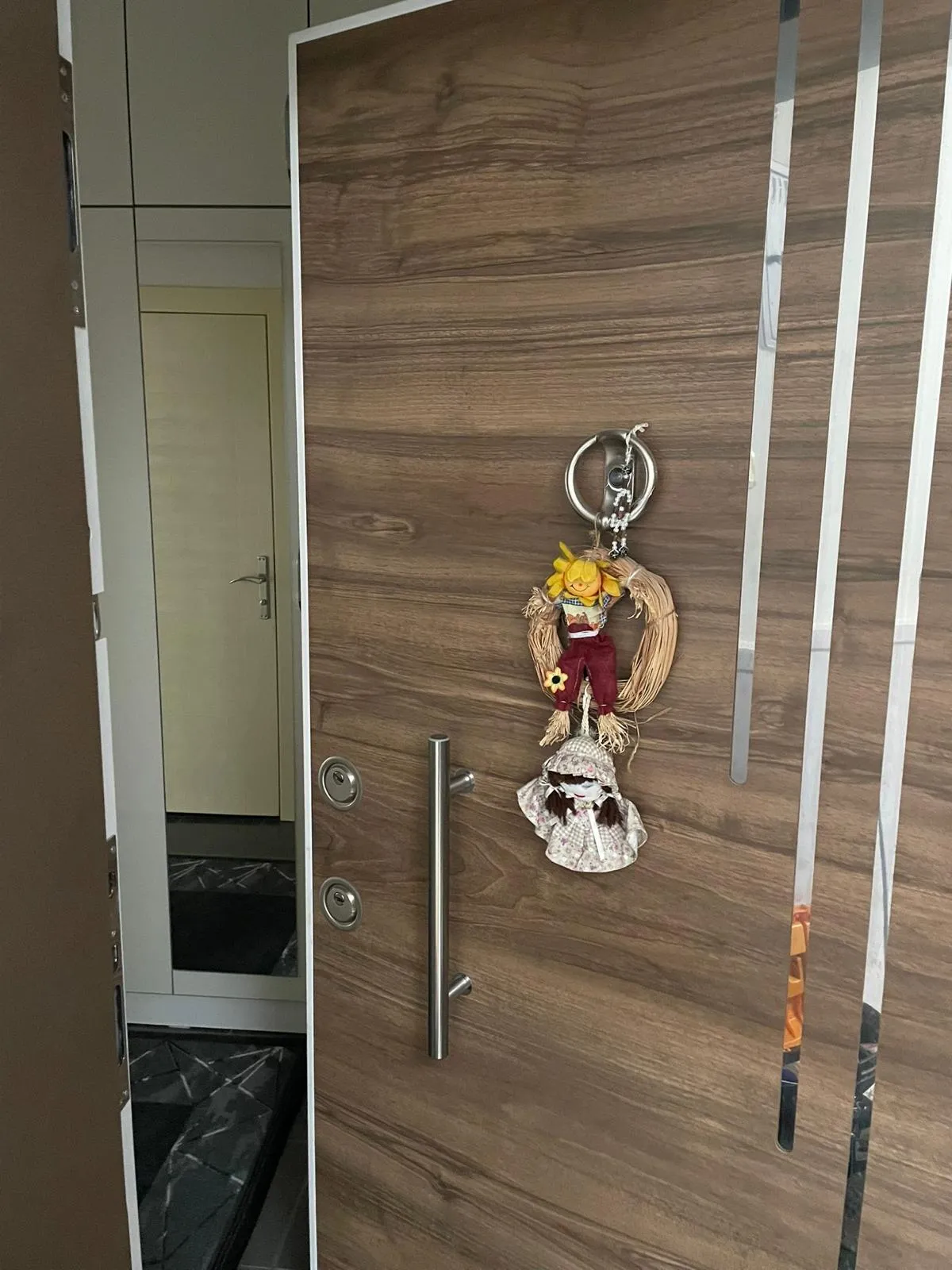 Ahşap desenli çelik kapının yüzünde iki ayrı barel rozeti ve çelik boru kulp; kapı açık hâlde