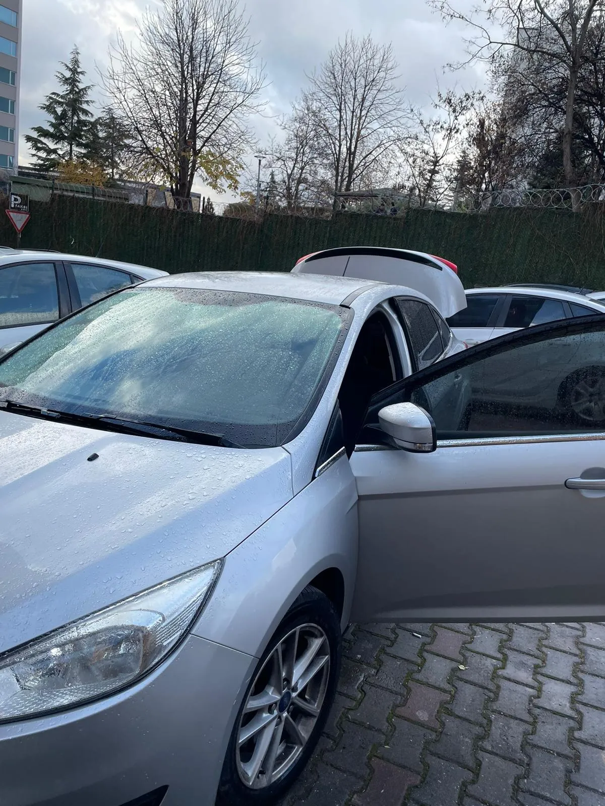 Yağmurlu havada otoparkta kapısı açılmış gri Ford Focus