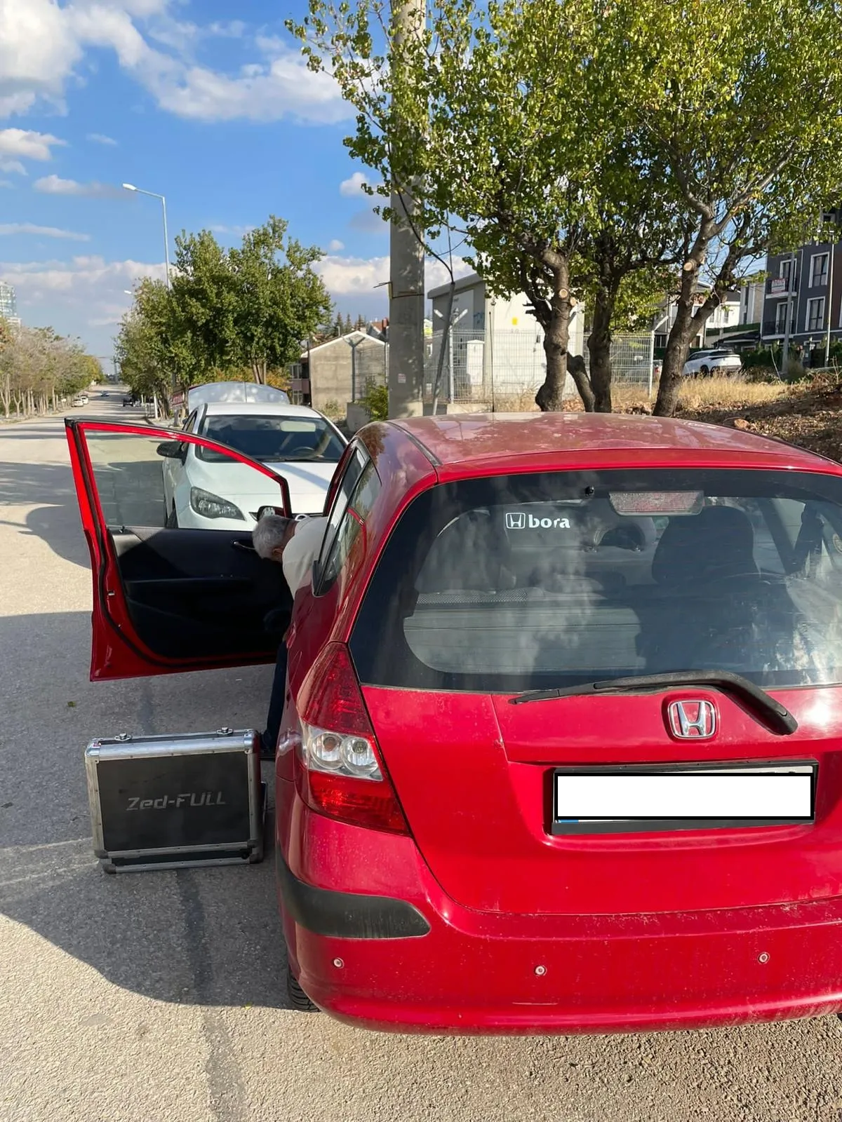 Kapısı açık kırmızı Honda Civic'in yanında yerde duran Zed-FULL anahtar kodlama cihazı çantası