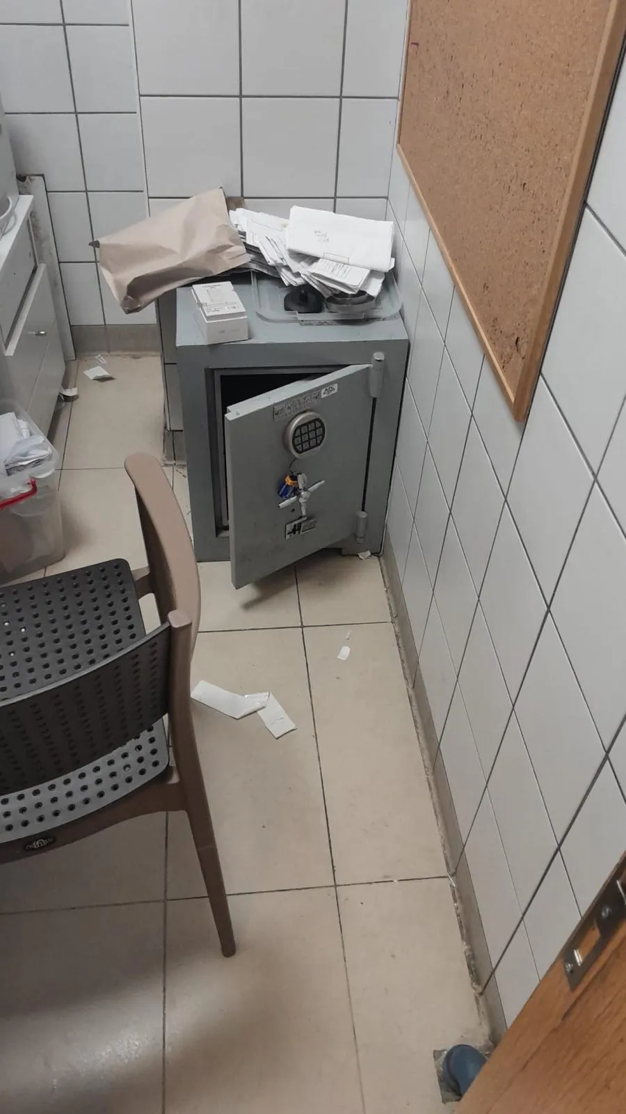 İş yerinde fayanslı bir odada kapağı aralanmış gri çelik kasa; kilidinde anahtar takılı, üzerinde evraklar duruyor