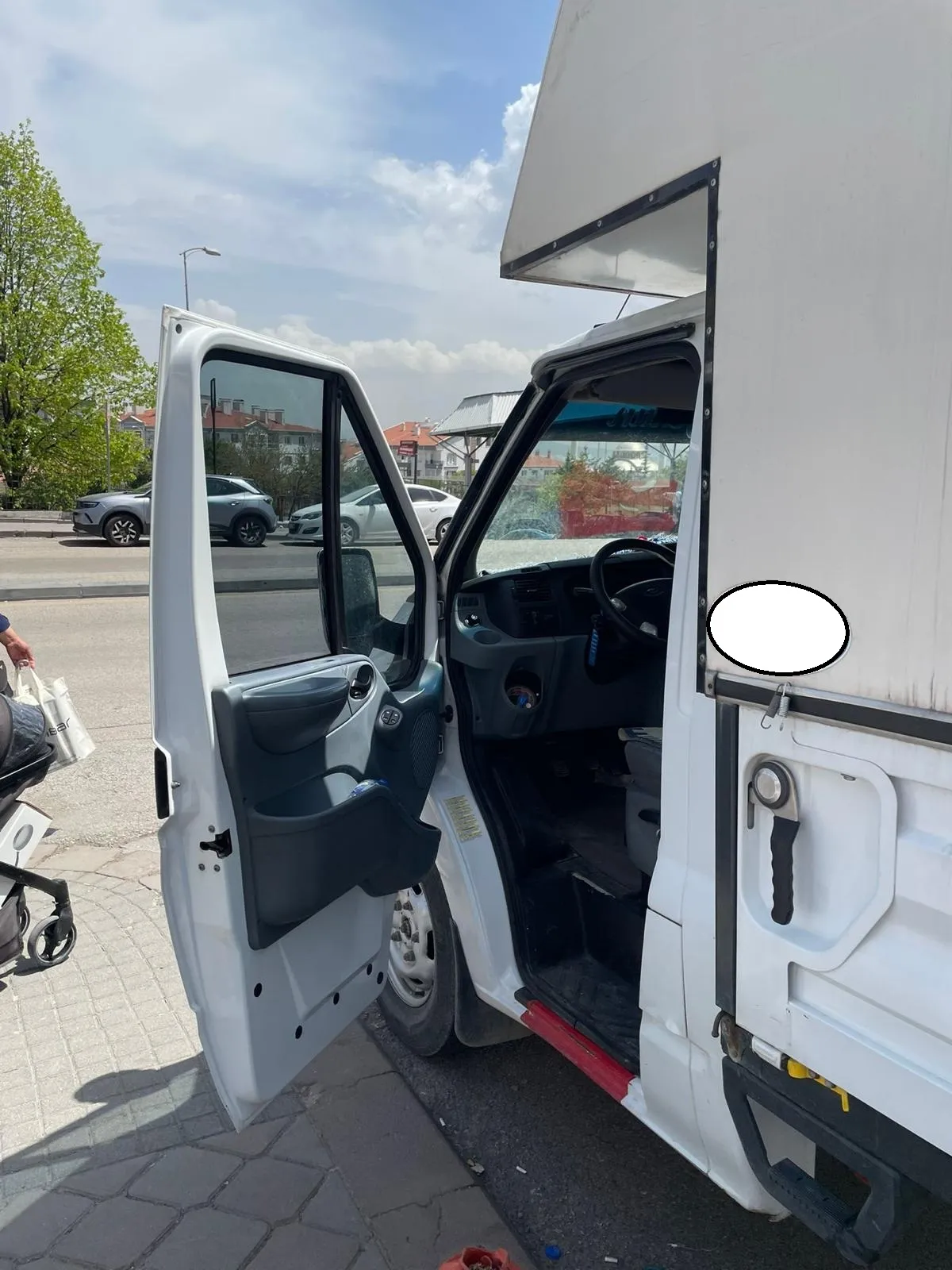 Cadde kenarında kabin kapısı açılmış beyaz Ford Transit kamyonet