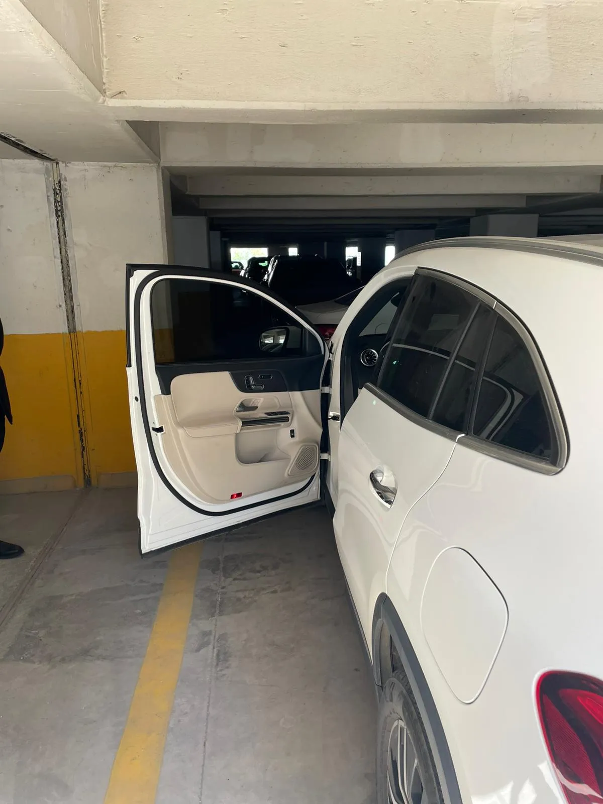 Kapalı otoparkta sarı şerit üzerinde kapısı açılmış beyaz Mercedes