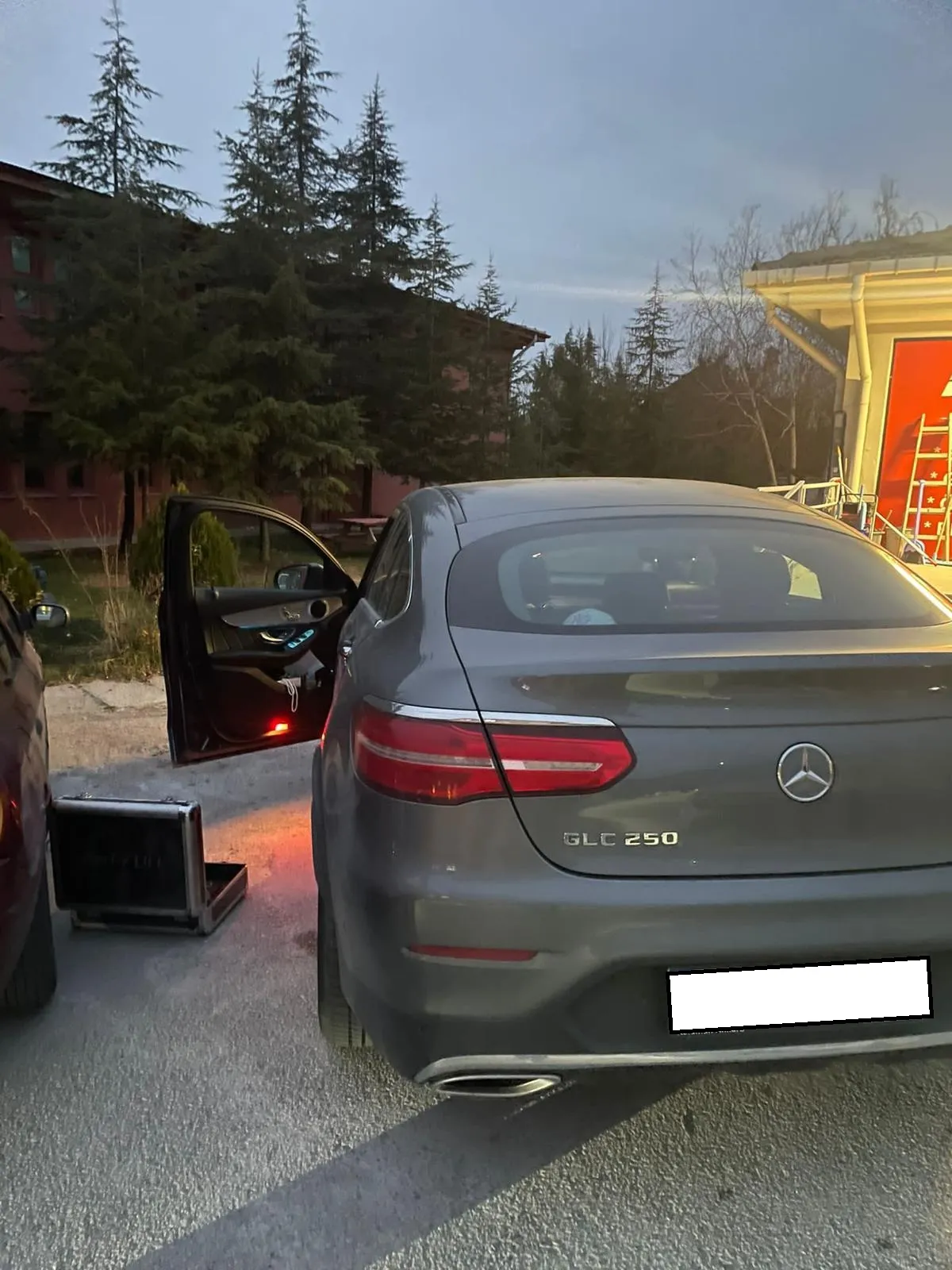 Alacakaranlıkta kapısı açık gri Mercedes GLC 250 Coupé ve yanında anahtar kodlama cihazı çantası