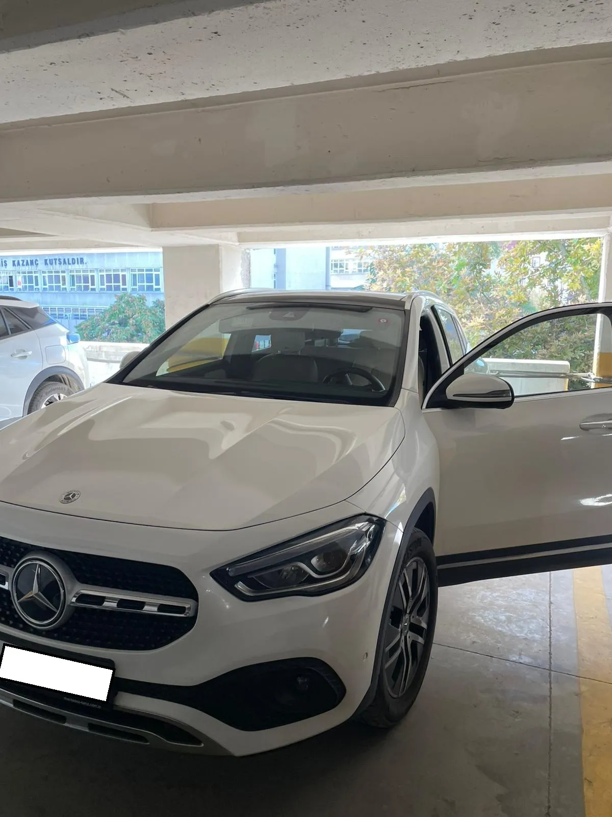 Üstü kapalı otoparkta sürücü kapısı açık beyaz Mercedes GLA