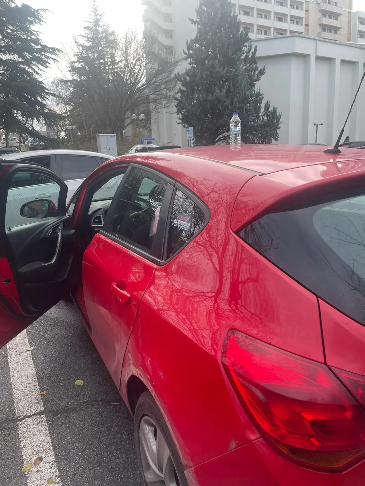 Otoparkta sürücü kapısı açılmış kırmızı Opel Corsa