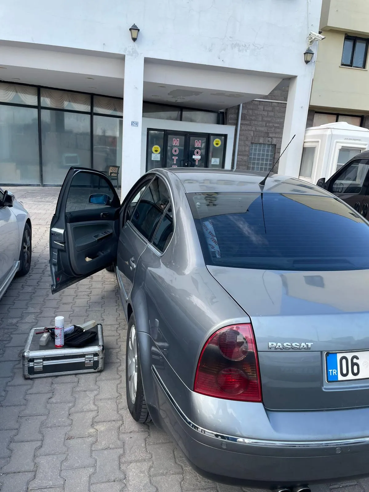 Kapısı açık gri Volkswagen Passat ve yanında yere konmuş, içi görünen çilingir alet çantası