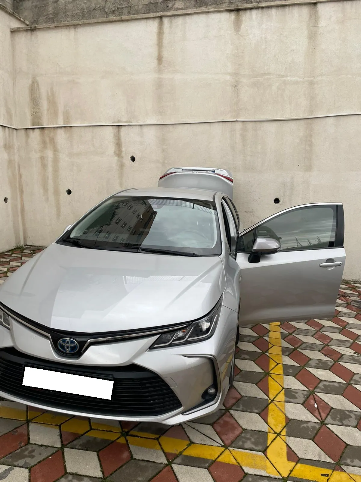 Otopark alanında sürücü kapısı açık gümüş renkli Toyota Corolla Hybrid
